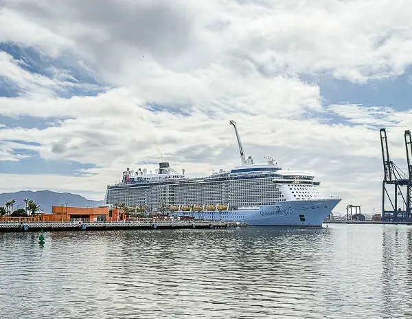 Royal Caribbean’s Quantum of the Seas docked in Ensenada, Mexico, with the ship’s North Star observation pod raised above the top deck. The port buildings, cranes, and cloudy sky frame the waterfront.