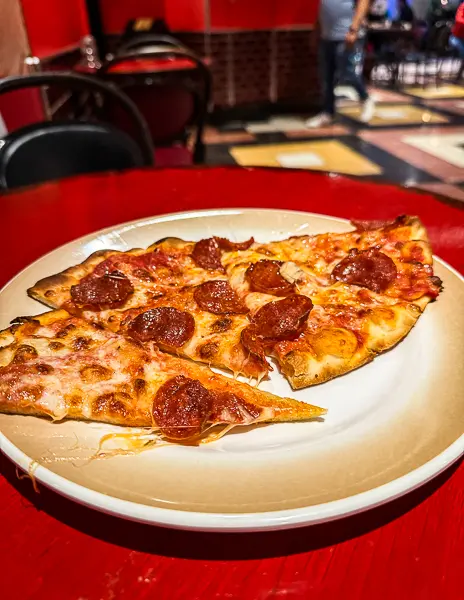 Plate of pepperoni pizza slices from Sorrento’s on Quantum of the Seas, sitting on a red table with the colorful tiled flooring and dining area in the background.