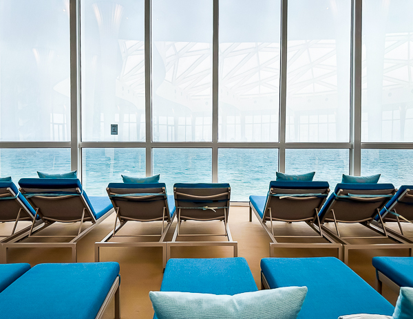 Empty lounge chairs with ocean views inside a cruise ship observation lounge during a sea day before crowds arrive.