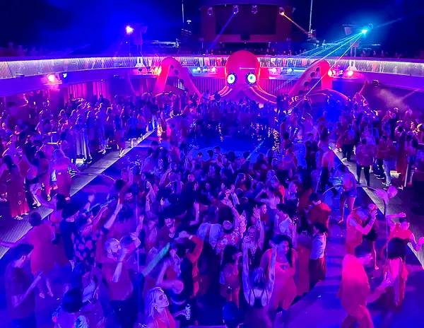 Crowds dancing during Scarlet Night on a Virgin Voyages cruise ship, showing guests participating in one of the most popular sea day evening events onboard.