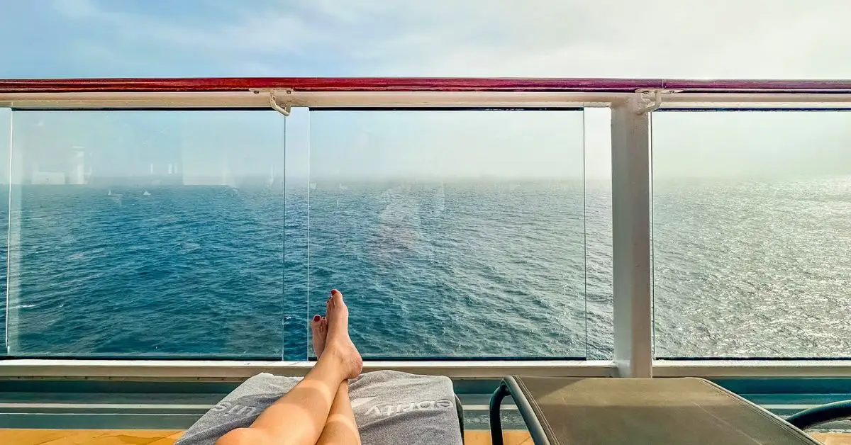 featured image: Relaxing sea day on a cruise with ocean views from a deck lounge chair and glass railing.