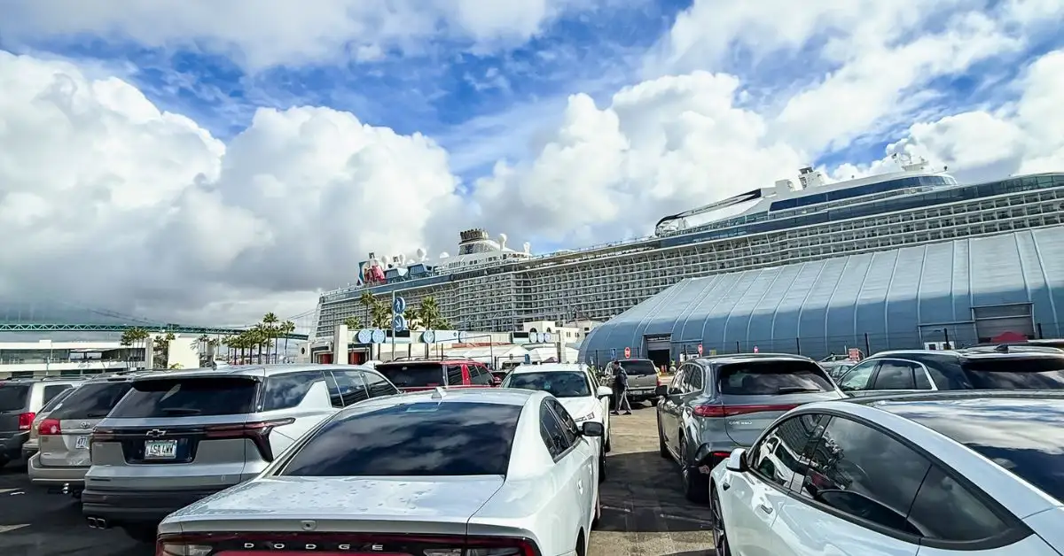 featured image: Cars parked at a cruise terminal with a ship docked behind them, capturing what it looks like when you’re cruising from your homeport instead of flying.