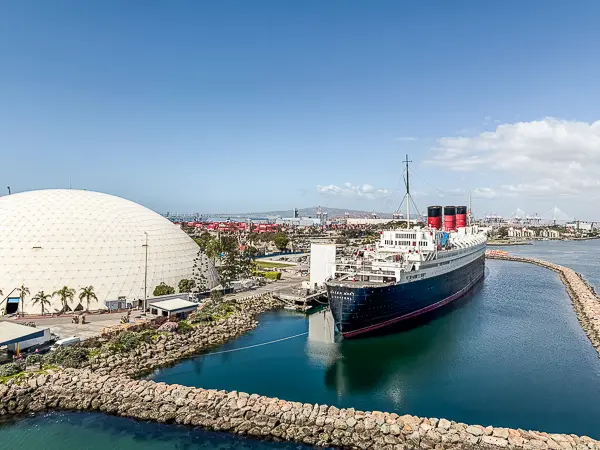 View from a cruise ship of the Long Beach Cruise Terminal dome and the Queen Mary docked beside it.