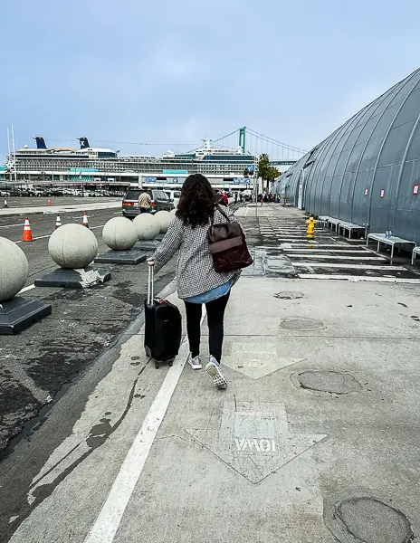 Person (Kathy) walking with luggage toward the cruise terminal after parking at the port, showing the convenience of arriving for a homeport sailing without needing a hotel stay.