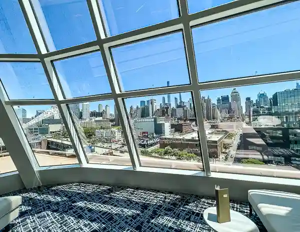 View from inside a cruise terminal with large glass windows looking out over a city skyline and port area, showing seating and bright daylight before embarkation.