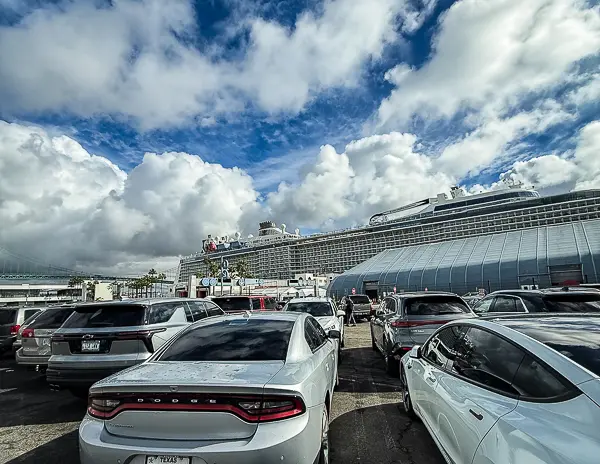 Cars parked in a cruise terminal lot with the ship in view, showing the convenience of driving to your local homeport instead of flying.
