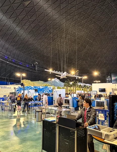 Security screening area inside Carnival’s Long Beach Cruise Terminal dome, with passengers going through metal detectors and staff assisting travelers.