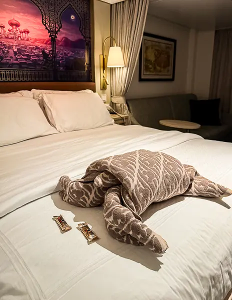 Disney cruise stateroom bed with towel animal made from throw blanket and Dove chocolates during turn-down service.
