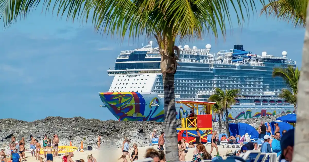 Norwegian Encore docked at Great Stirrup Cay, with beachgoers on the island and palm trees in the foreground during a Norwegian Cruise Line visit.