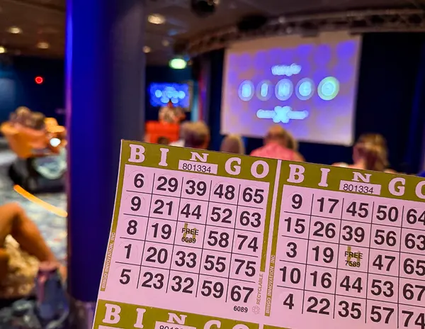 Cruise ship bingo game in progress during a sea day, with bingo cards held up in a theater and the game screen visible in the background.