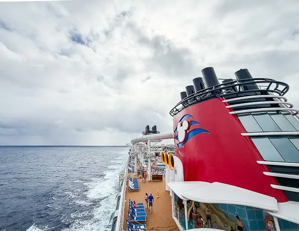 View from the upper deck of a Disney cruise ship at sea with the red funnel and ocean stretching into the distance.