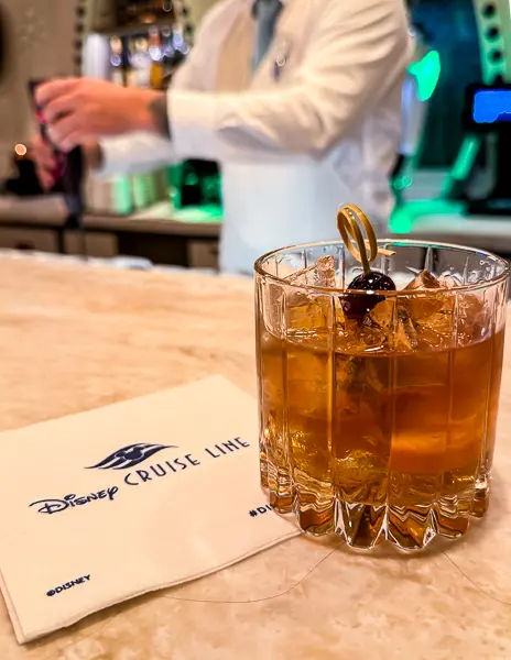 Old fashioned cocktail served at a Disney Cruise Line bar with bartender in background.