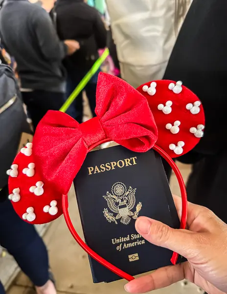 Hand holding a United States passport with red Mickey Mouse ears headband, taken during Disney cruise check-in.