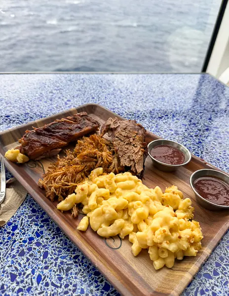 Barbecue platter with ribs, pulled pork, brisket, mac and cheese, and sauces from Mickey’s Smokestack Barbecue on Disney Treasure.