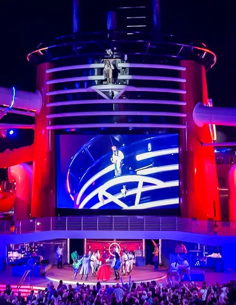 Captain Jack Sparrow appearing above the stage during Pirate Night on Disney Treasure with performers below and guests gathered on deck.
