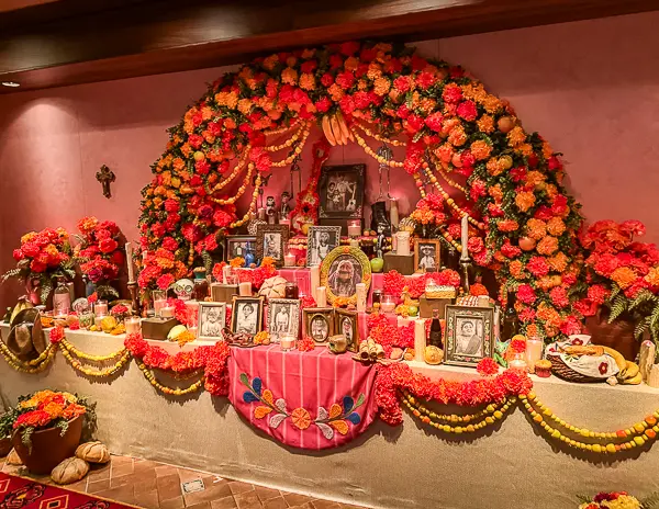 Día de los Muertos ofrenda inside Plaza de Coco on Disney Treasure featuring framed photos, marigold flowers, candles, and vibrant decorations.