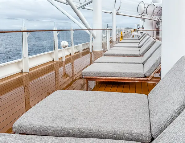 Row of cushioned lounge chairs along the Quiet Cove adults-only deck on Disney Treasure with ocean views.
