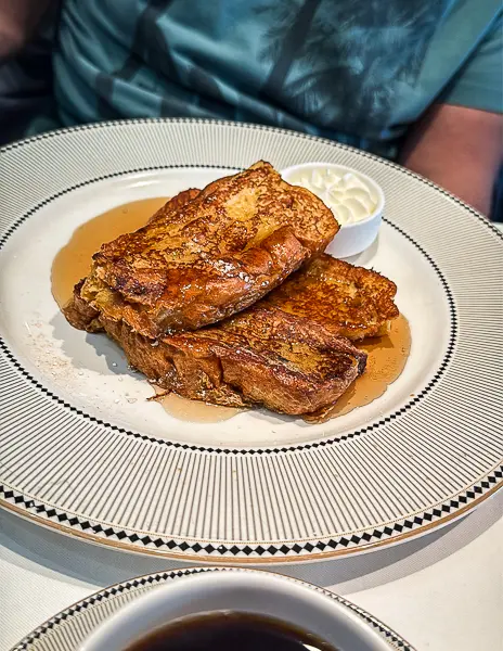 Brioche French toast at 1923 on Disney Treasure topped with powdered sugar and served with syrup and butter.