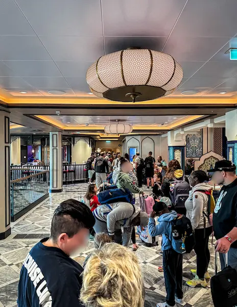 Guests lined up with luggage during debarkation on Disney Treasure, waiting in the hallway to exit the ship.