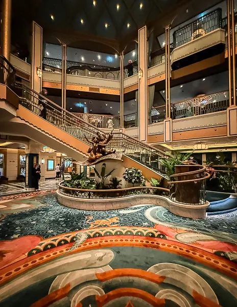 Grand Hall interior on Disney Treasure featuring the Aladdin statue at the base of the sweeping staircase.