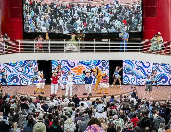 Disney characters including Mickey Mouse, Donald Duck, Daisy Duck, and Pluto performing on stage during the Disney Treasure sailaway party as guests watch from the deck.