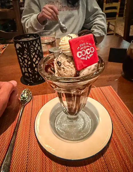 Featured ice cream sundae at Plaza de Coco on Disney Treasure topped with whipped cream and a themed chocolate square.