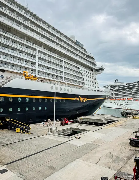 Disney Treasure docked at Port Canaveral before embarkation, with the ship’s name visible on the hull and another cruise ship in the background.