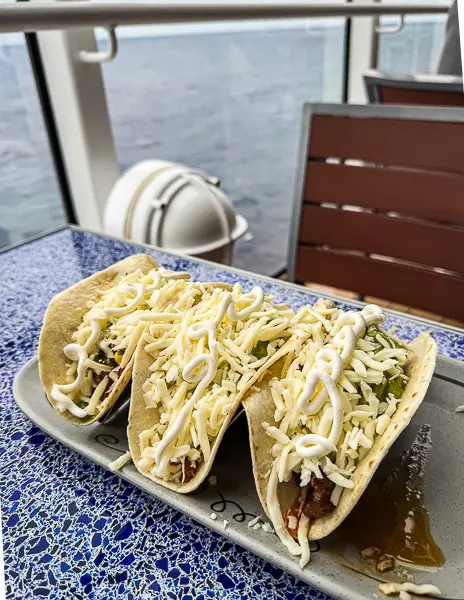 Soft tacos topped with shredded cheese and sauce from Donald’s Cantina on Disney Treasure.