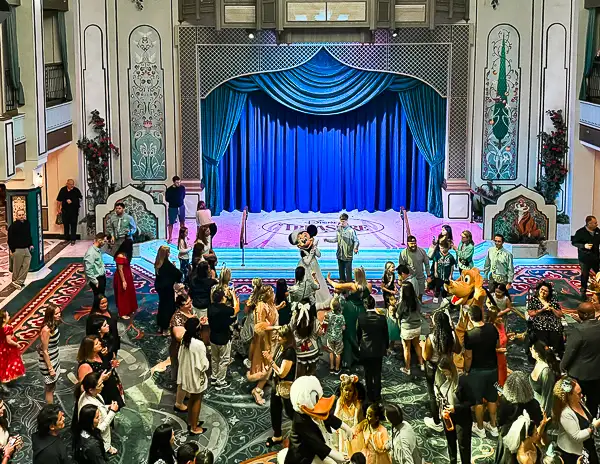 Guests dancing with Disney characters in the Grand Hall atrium during a lively onboard party on a Disney Cruise Line ship.
