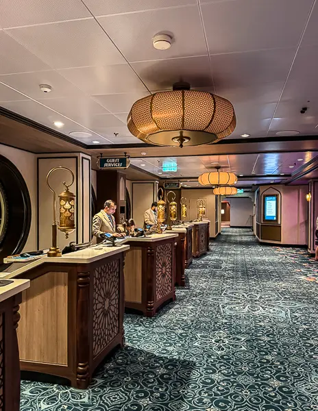 Disney Cruise Line Guest Services desk with cast members assisting guests in an elegant hallway onboard the Disney Treasure cruise ship.