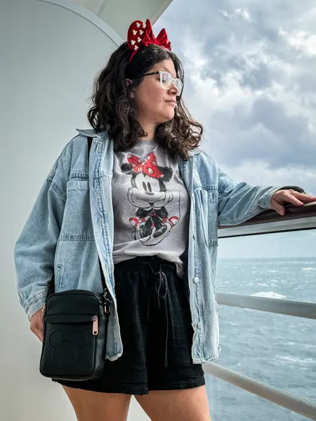 Disney cruise outfit with Minnie Mouse t-shirt, denim jacket, black shorts, and Minnie ears on deck