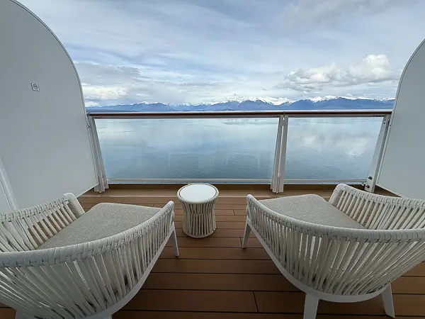 Empty cruise ship balcony overlooking calm water and snow-covered mountains during an Alaska cruise.