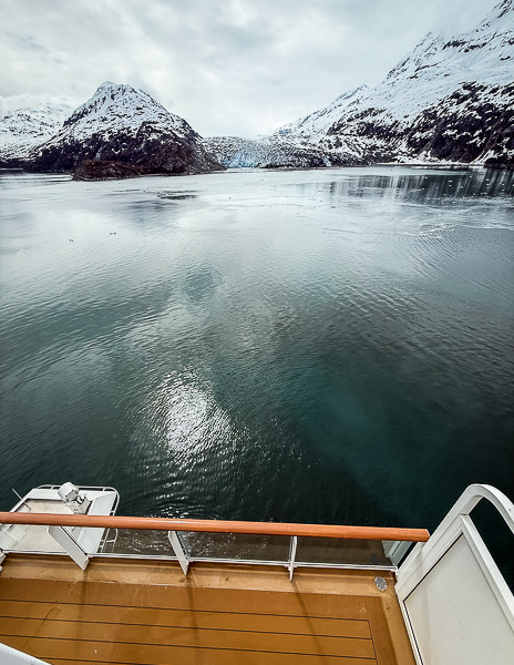 Glacier scenery with calm water and snow-covered mountains viewed from a cruise ship balcony area during an Alaska cruise.