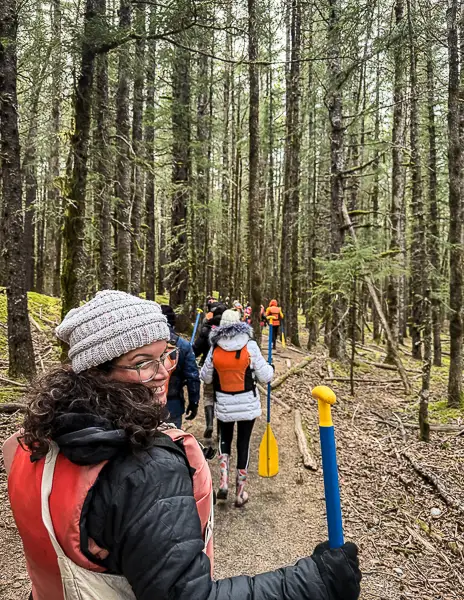 Kath carrying a paddle while walking through the forest during the Glacier Point Wilderness Safari from Skagway.