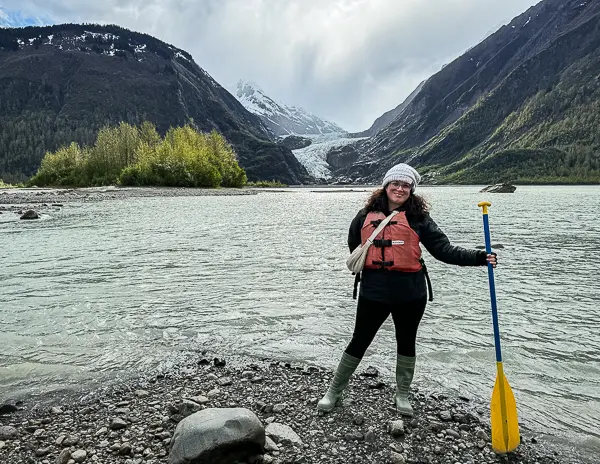 Kathy wearing rubber boots and a life vest while holding a paddle near Davidson Glacier