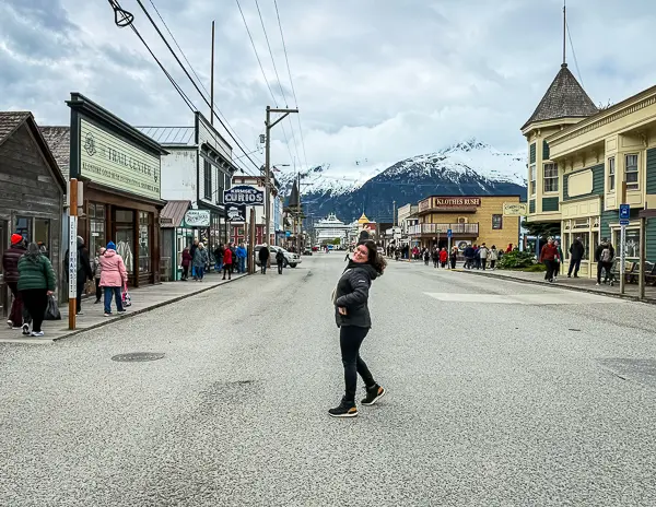 Kathy walking through downtown Skagway during an Alaska cruise port day, with shops and snowcapped mountains in the background.