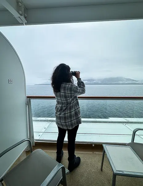 Woman (Kathy) using binoculars from a cruise ship balcony while sailing in Alaska.