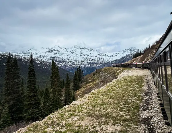 View from the White Pass train ride from Skagway, Alaska, with snowcapped mountains, evergreen trees, and the train curving along the tracks during an Alaska cruise excursion.