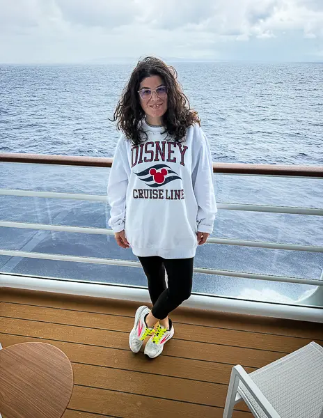Woman (kathy) wearing Disney Cruise Line sweatshirt with black leggings and sneakers on a Disney cruise ship cabin balcony