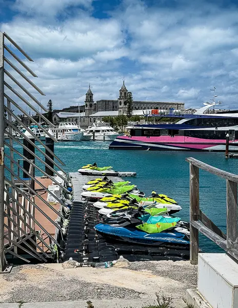 Jet skis lined up at the Bermuda cruise port in Royal Naval Dockyard, with the marina, ferry, and Clocktower Mall in the background.