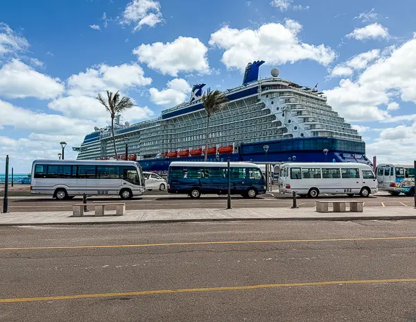 Shuttles lined up outside the Bermuda cruise port at Royal Naval Dockyard with a Celebrity cruise ship in the background.