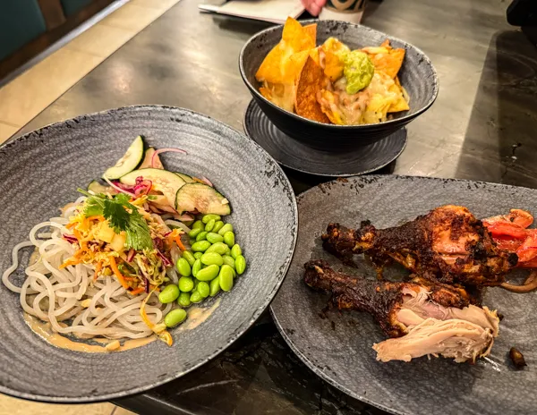 Assorted dishes from Indulge Food Hall on Norwegian Aqua, including roasted chicken, noodles, edamame, and chips.
