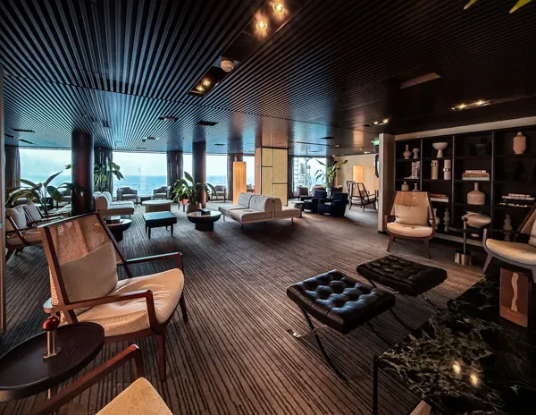 Seating area inside Norwegian Aqua The Haven Lounge with chairs, sofas, dark wood accents, and ocean views.