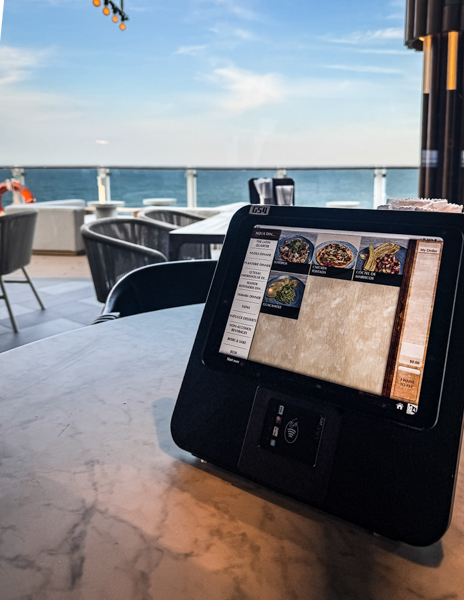 Ordering tablet at Indulge Food Hall on Norwegian Aqua with menu items and ocean views in the background.