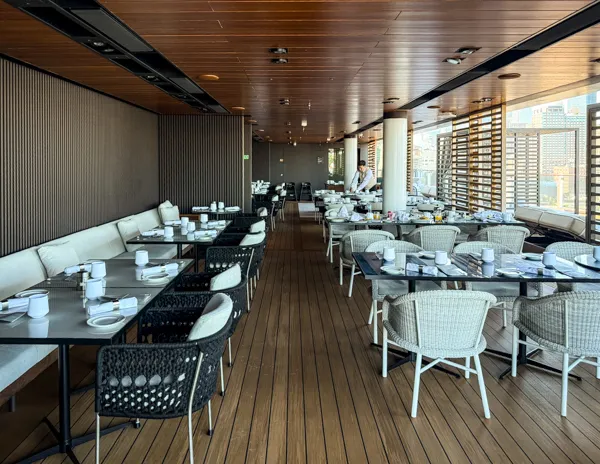 Outdoor dining area on Norwegian Aqua The Haven pool deck with tables set for breakfast and city views.