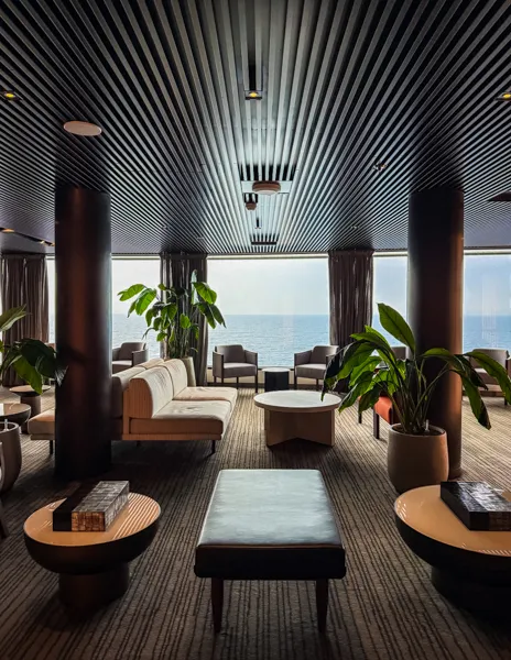 Norwegian Aqua The Haven Lounge with seating, plants, and ocean views through floor-to-ceiling windows.