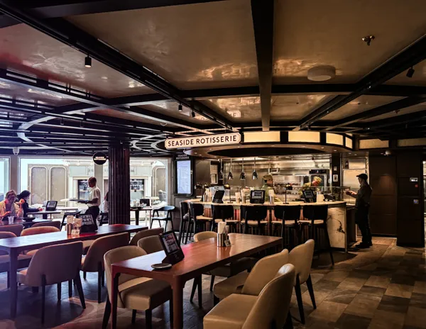 Seaside Rotisserie food station and tables inside Indulge Food Hall on Norwegian Aqua.