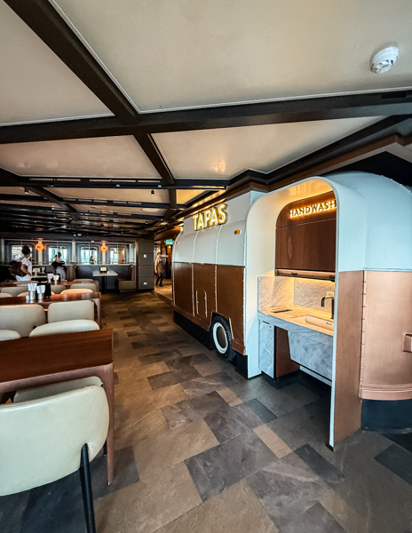 Tapas food station inside Indulge Food Hall on Norwegian Aqua with nearby seating and handwashing station.