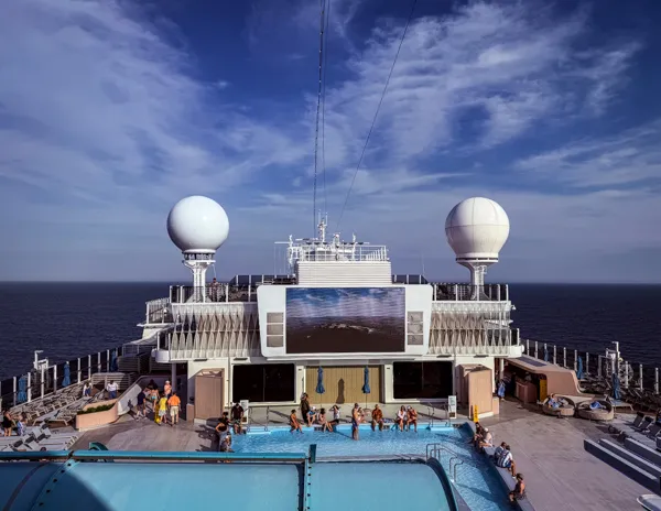Norwegian Aqua main pool deck from above with pool, large screen, loungers, and ocean views.