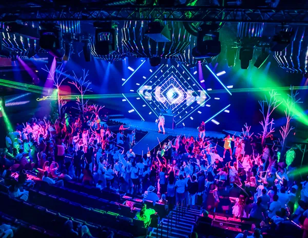 GLOW party inside the Norwegian Aqua theater with colorful lights and passengers dancing.